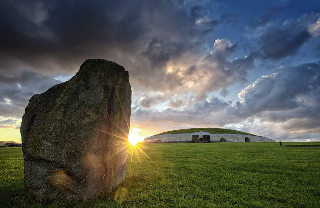 Sunrise illuminates Newgrange passage tomb and standing stone in County Meath.